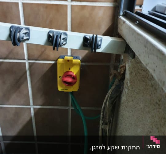 מתג חשמלי צהוב עם כבל ירוק על קיר אריחים